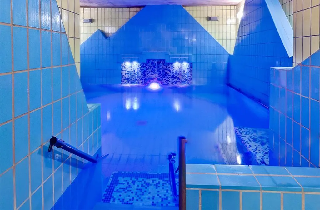 Piscina termale interna con piastrelle blu e mosaici, illuminazione soffusa