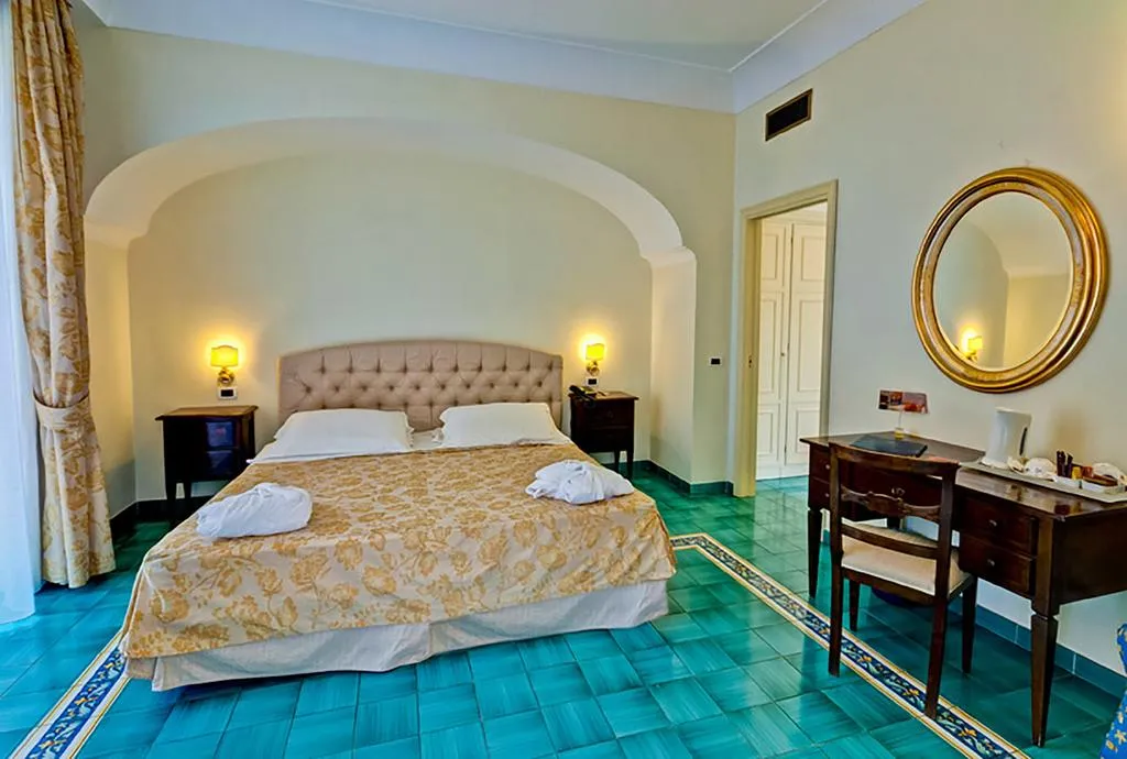 Camera spaziosa con letto matrimoniale, pavimento in maiolica verde, scrivania antica e specchio dorato