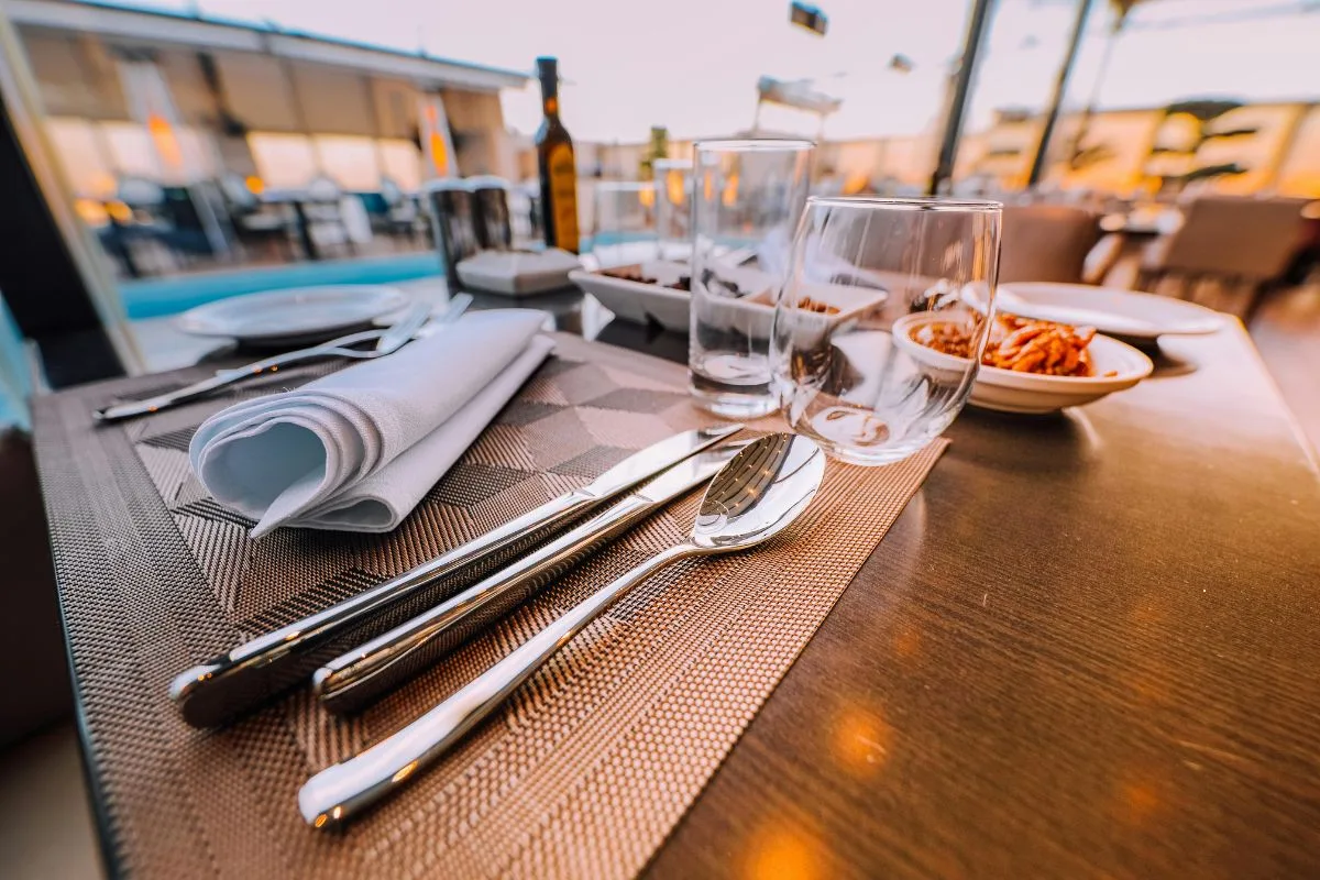 Tavolo del ristorante apparecchiato con posate, bicchieri e tovagliolo al tramonto