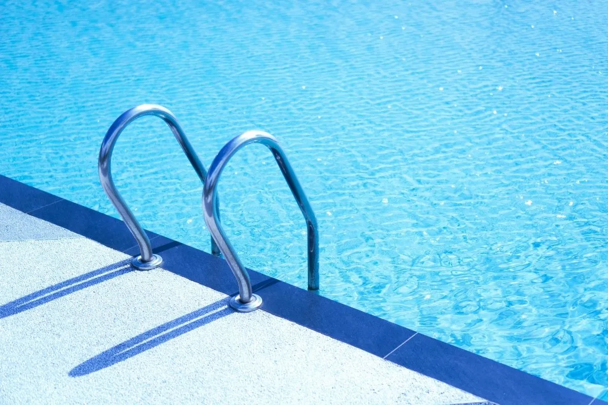 Scaletta in acciaio inox a bordo di una piscina esterna con acqua turchese