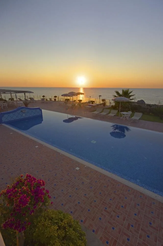 Piscina esterna con terrazza, lettini e ombrelloni affacciata sul mare al tramonto